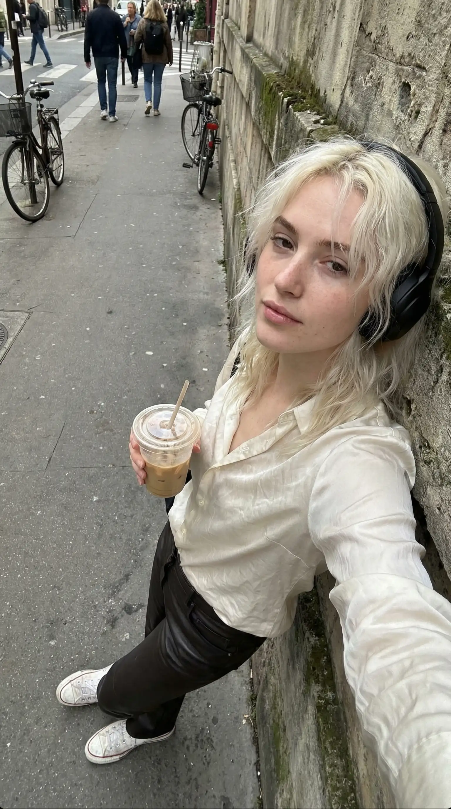 Street selfie of a woman with headphones and an iced coffee